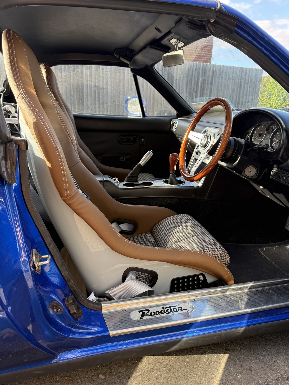 MX-5 interior with a tan Mirco bucket seat, wooden Nardi steering wheel and chrome Roadster sill plate