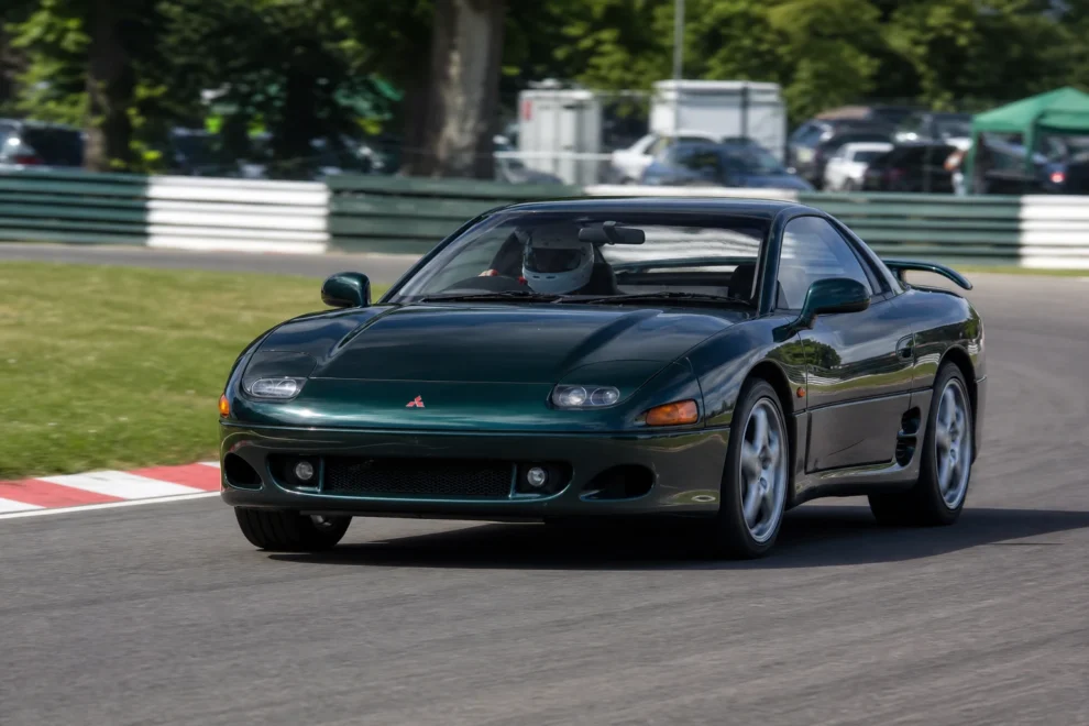 A dark green Mitsubishi GTO, the Japanese market 3000GT, cornering on a UK circuit with a helmeted driver
