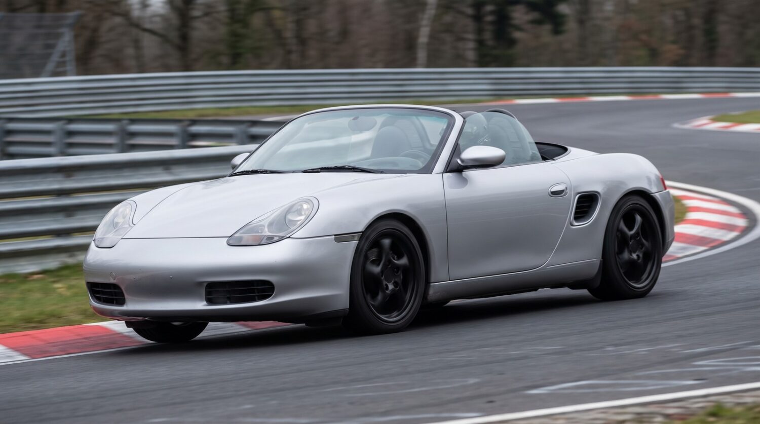 Silver Porsche Boxster 986 roadster cornering at an apex on a British race circuit with the roof down