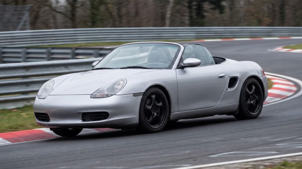 Silver Porsche Boxster 986 roadster cornering at an apex on a British race circuit with the roof down
