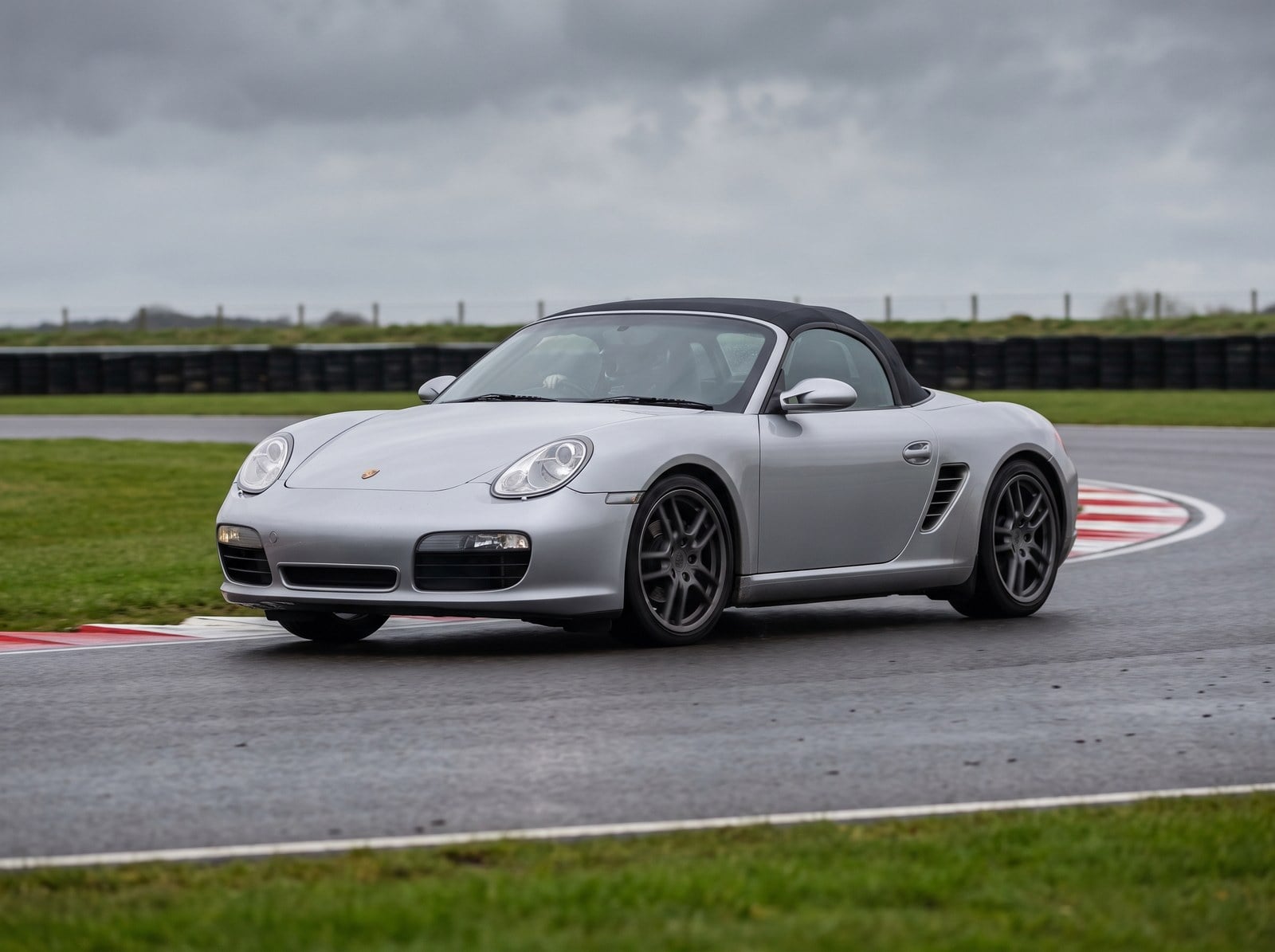 Silver Porsche Boxster 987 on a British circuit with the roof up