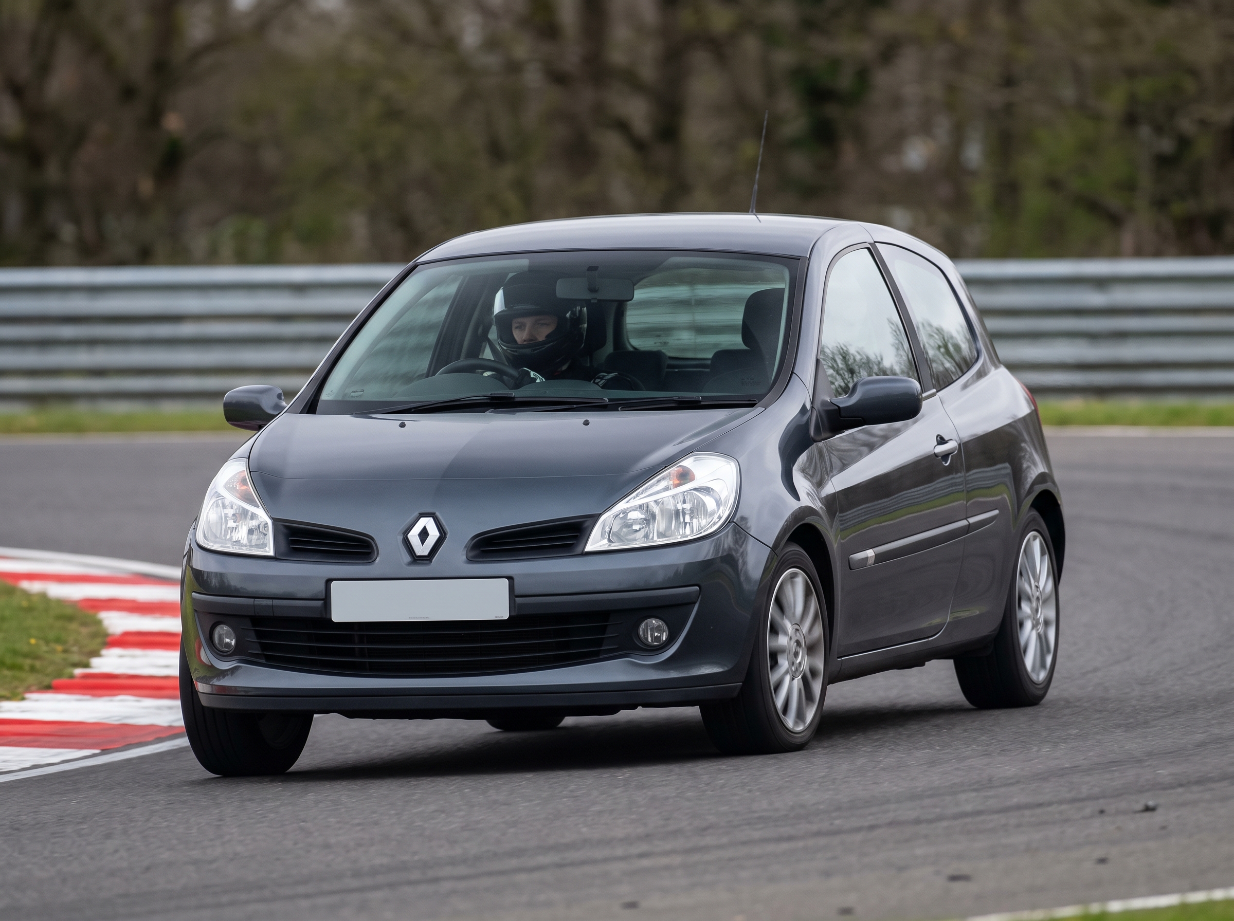 Grey Renault Clio Mk3 hatchback on a British race circuit at an apex with red and white kerbing