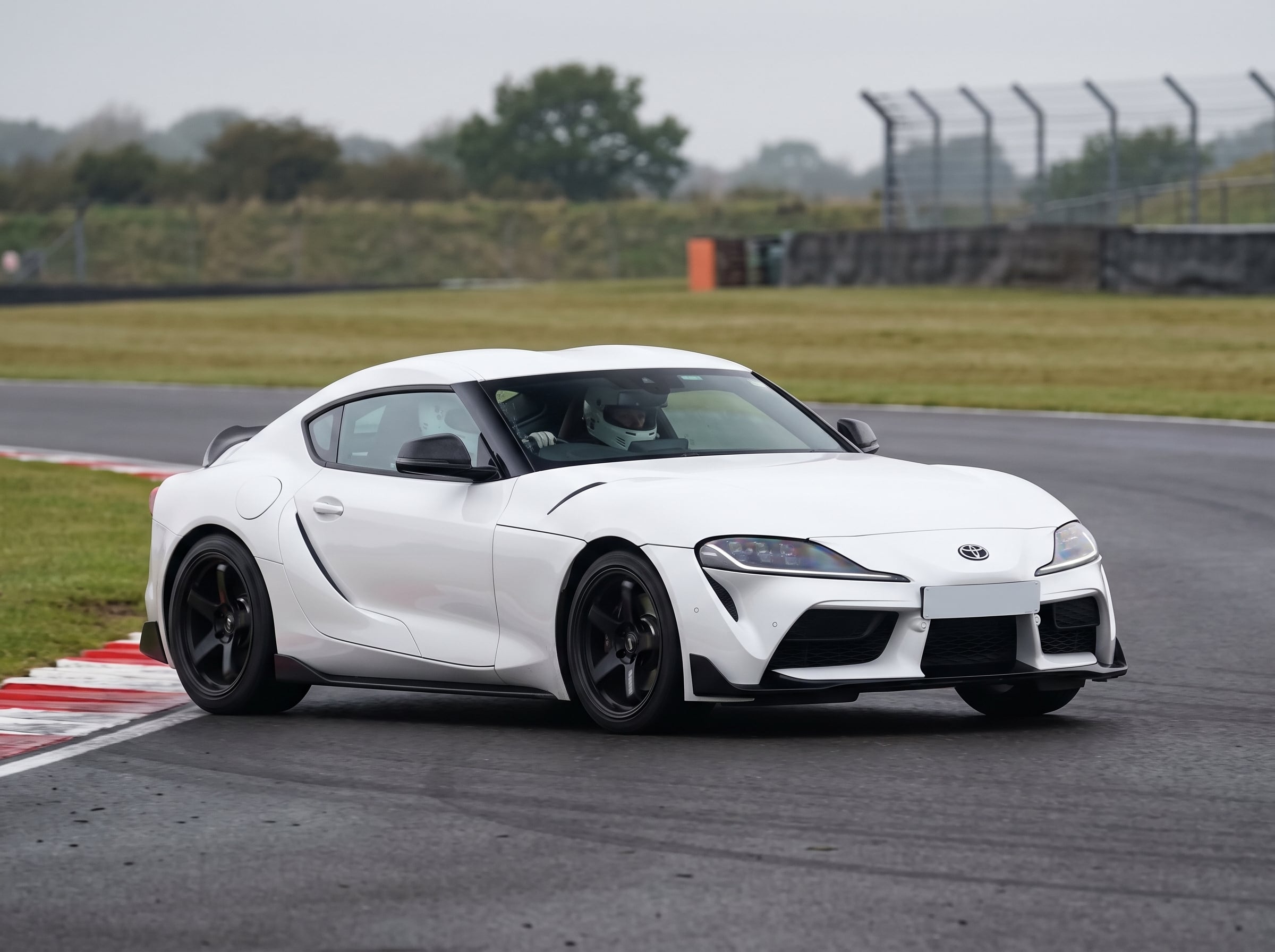 White Toyota Supra A90 on a British race circuit at an apex with red and white kerbing