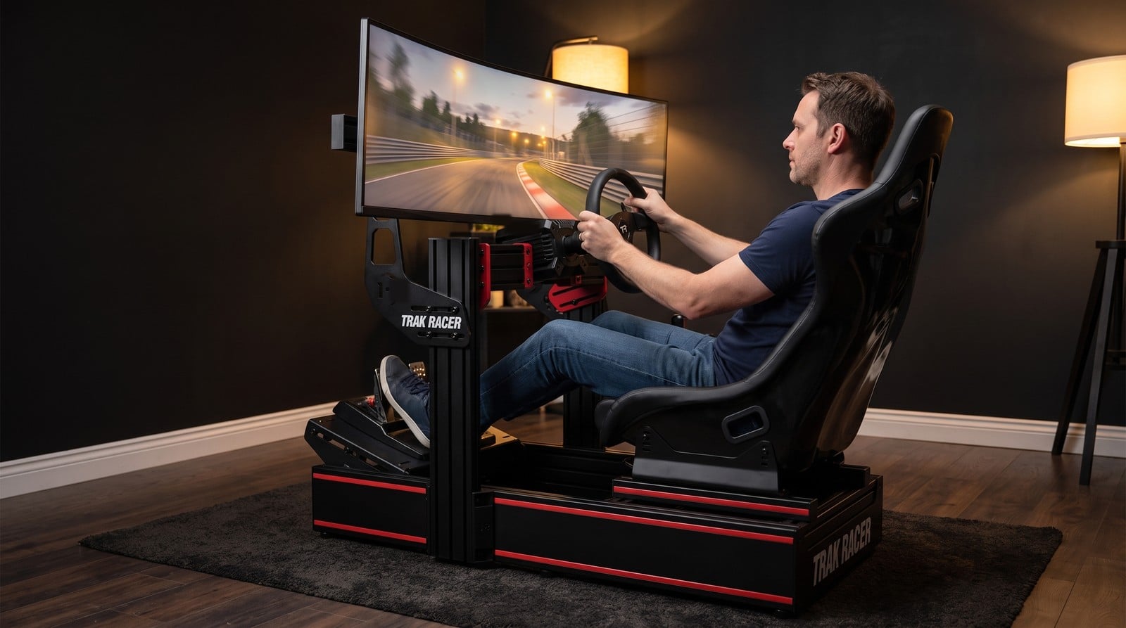 Driver mid-race on a Trak Racer TR160 aluminium extrusion sim rig with red accent stripes, fitted with a plain black bucket seat on side mount brackets under an ultrawide monitor