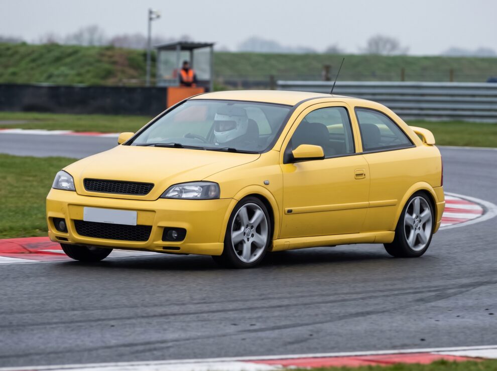 Yellow Vauxhall Astra Mk4 on a British race circuit at an apex with red and white kerbing