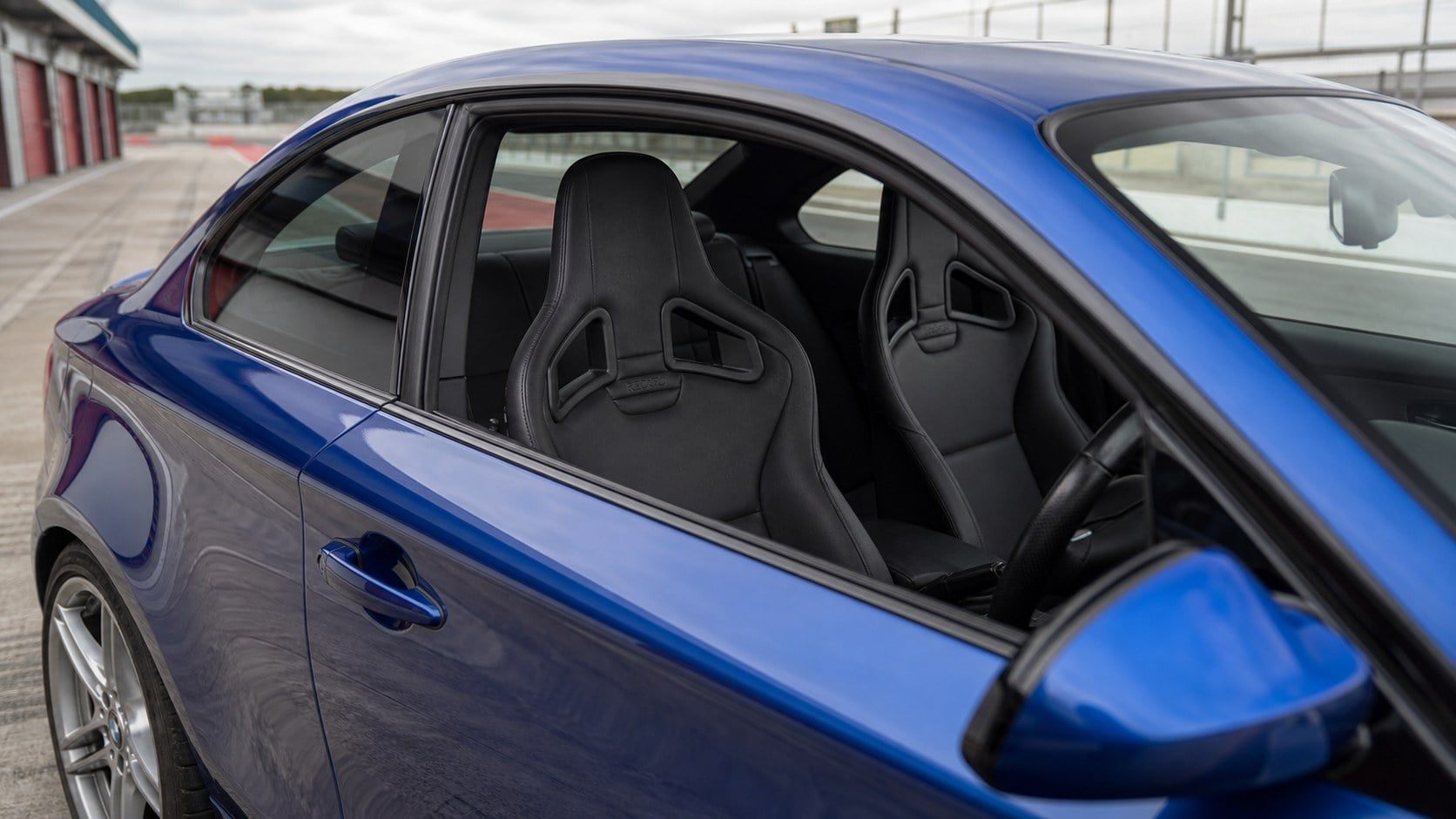 View through the right-hand driver window of a Le Mans blue BMW 135i E82 showing black Recaro Sportster CS seats