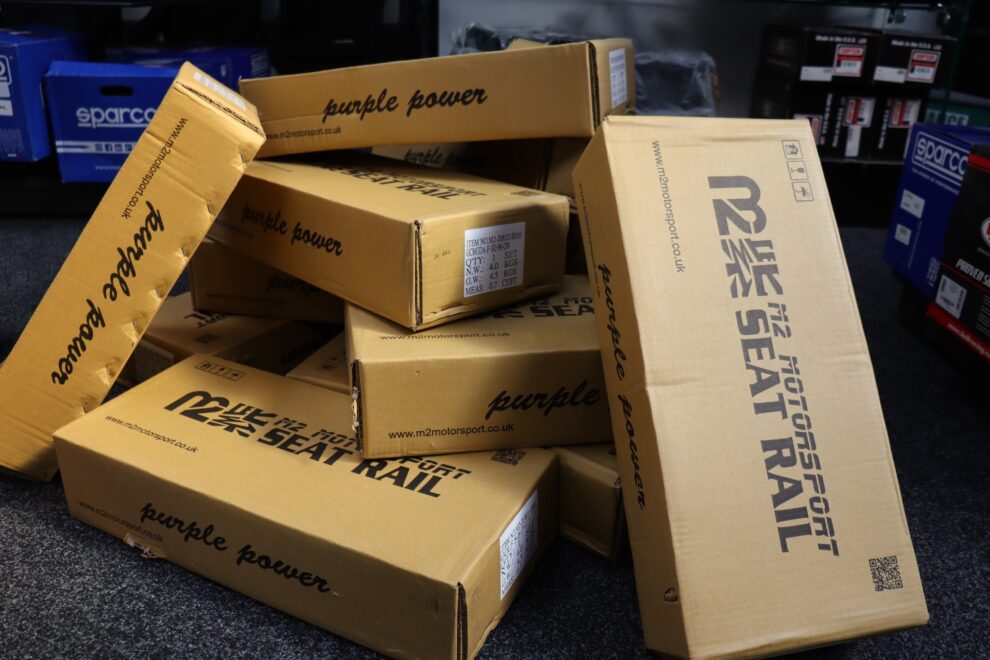 A pile of M2 Motorsport seat rail boxes in the GSM Performance showroom, the printed labels showing one set per box with left and right hand rails listed separately