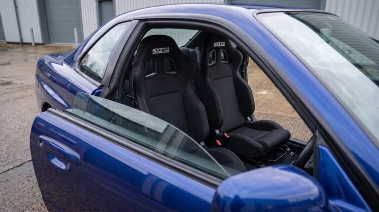 Pair of black Sparco R100 reclining seats with white Sparco headrest logos fitted in a blue Nissan Skyline R34