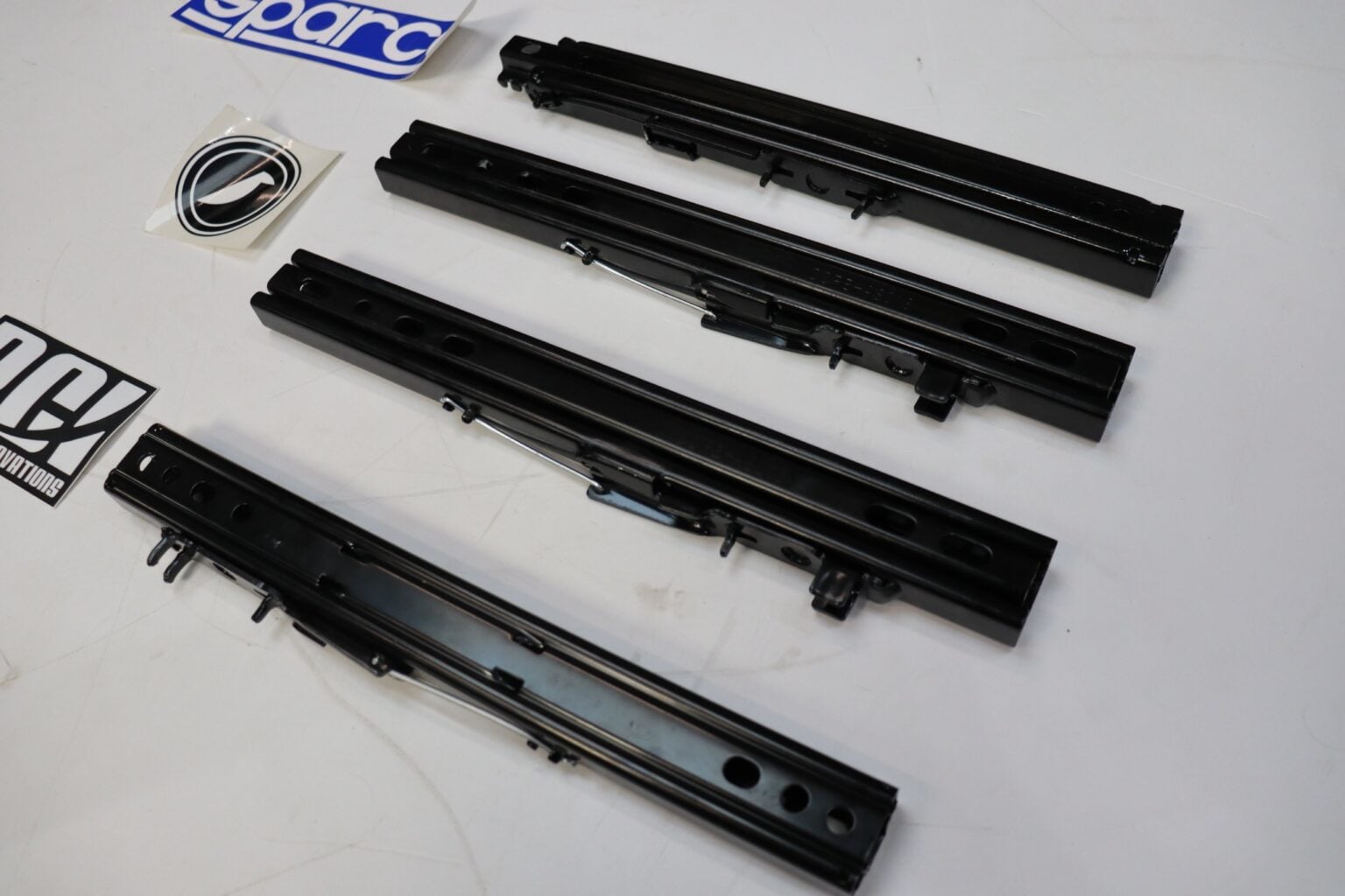 Seat sliding runner rails laid out at an angle beside PCI, Sparco and Corbeau brand stickers