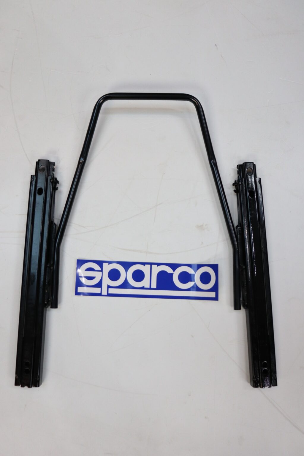 Complete Sparco seat sliding runner kit laid out as it sits under a seat, beside the Sparco sticker