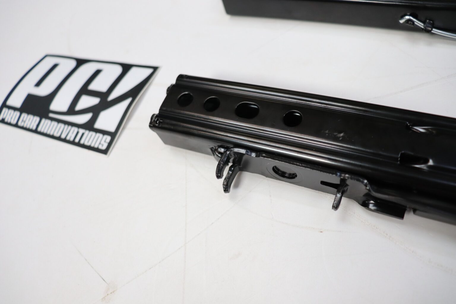 Close-up of a PCI Racing universal seat slider rail showing large lightening holes, beside the PCI Pro Car Innovations sticker