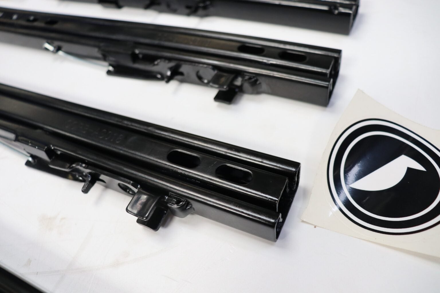 Close-up of a Corbeau seat sliding runner rail beside the Corbeau logo sticker
