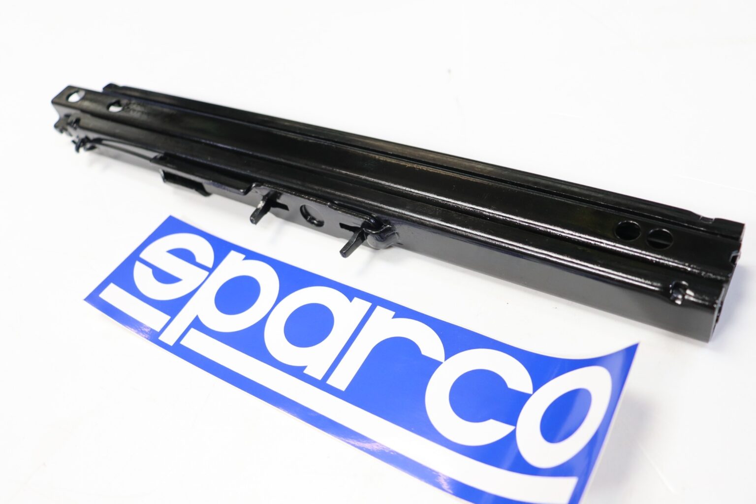 Close-up of a Sparco seat sliding runner rail beside the Sparco logo sticker