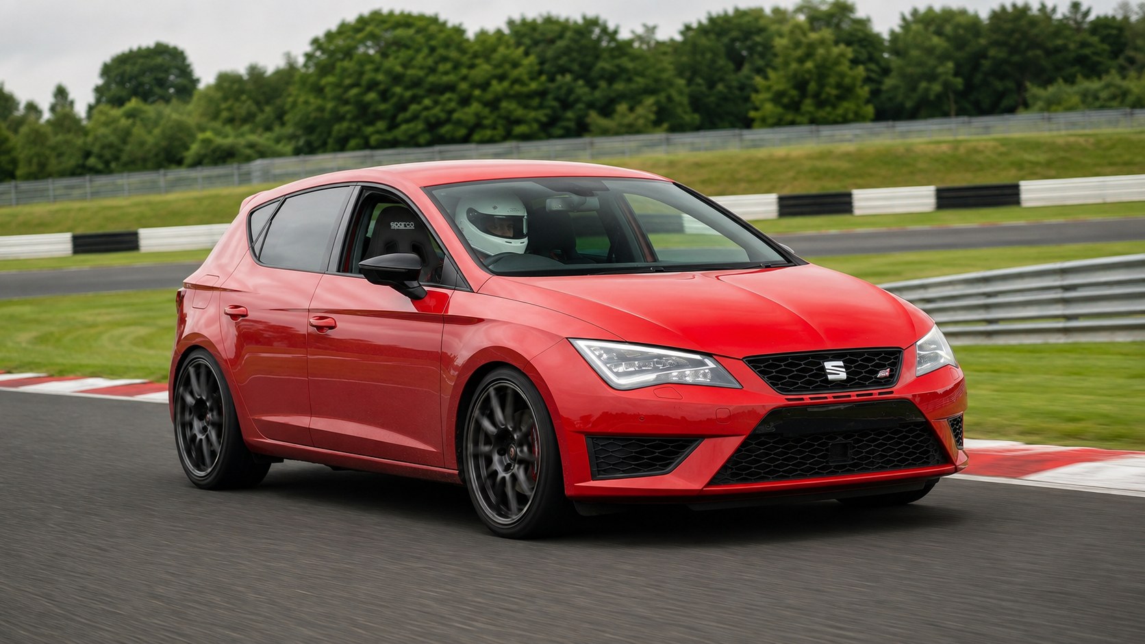 Helmeted driver in a red SEAT Leon Mk3 on track, seated in a black Sparco R500 reclining sport seat