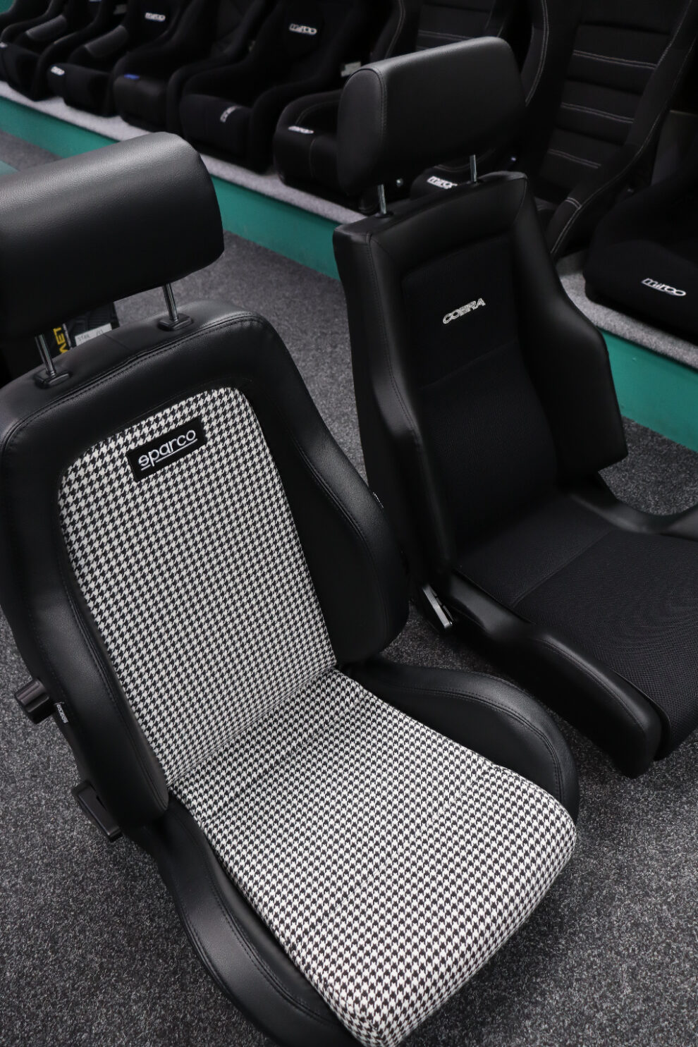 Sparco GT Houndstooth and Cobra Le Mans reclining seats side by side, three quarter view from the front with the Sparco in the foreground