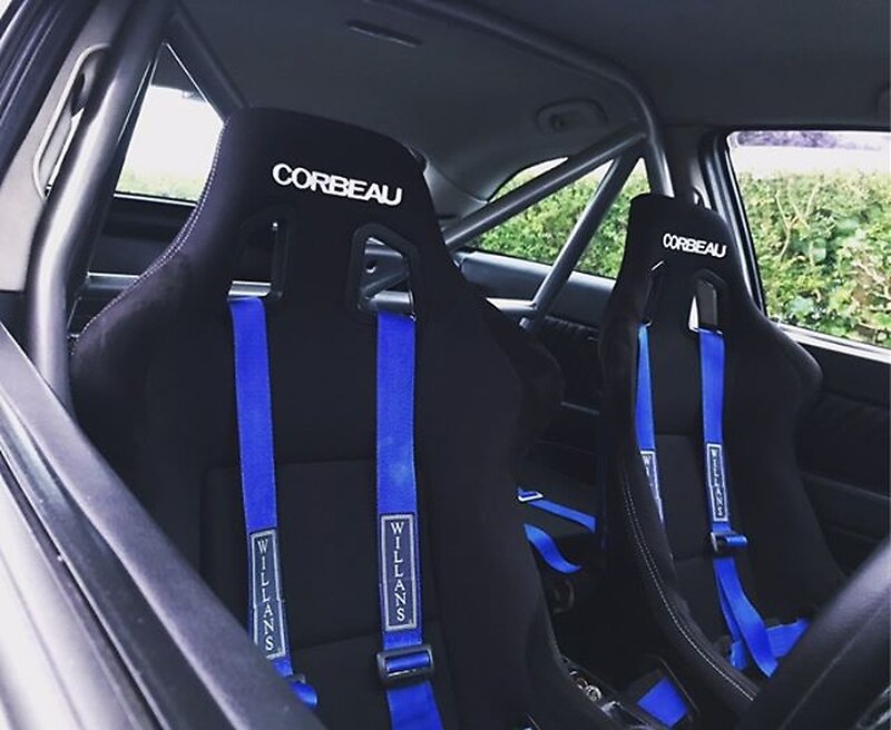 Two black Corbeau Clubsport bucket seats with blue Willans harnesses in a Vauxhall Astra with a silver roll cage