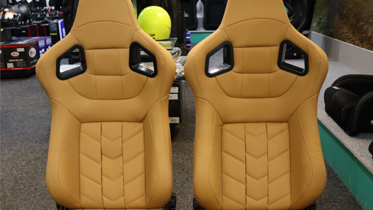A pair of beige vinyl Auto Style Type GK reclining sports seats with chevron stitching on the SportSeats4u showroom floor