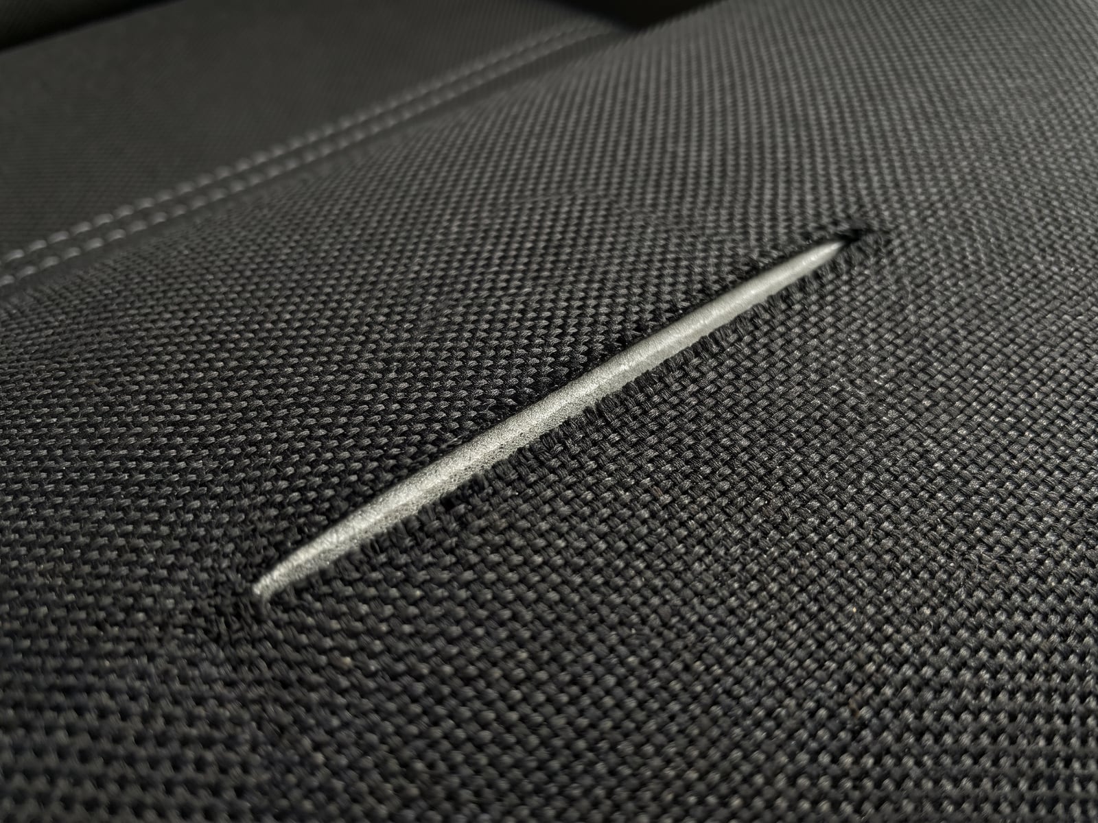 Illustration of a straight blade cut across black motorsport seat fabric with the yarn ends severed square and no fraying