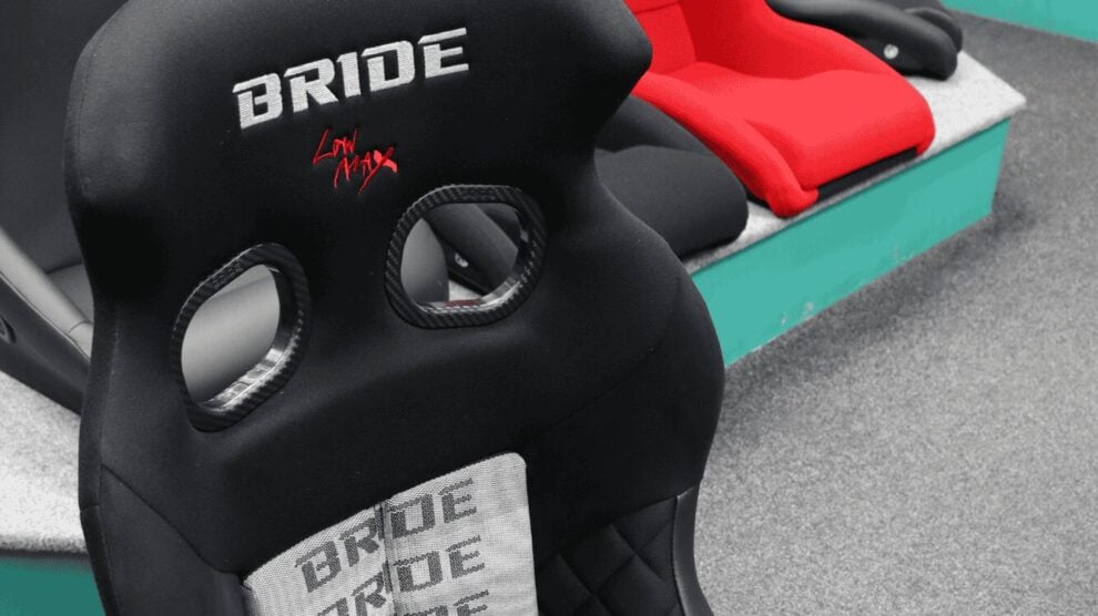 The back of a black Bride bucket seat with Low Max embroidery on the SportSeats4u showroom floor, with a red seat on the plinth behind