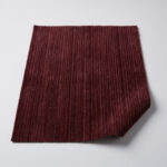 Swatch of burgundy fine wale corduroy upholstery fabric showing the narrow parallel ribs and soft nap