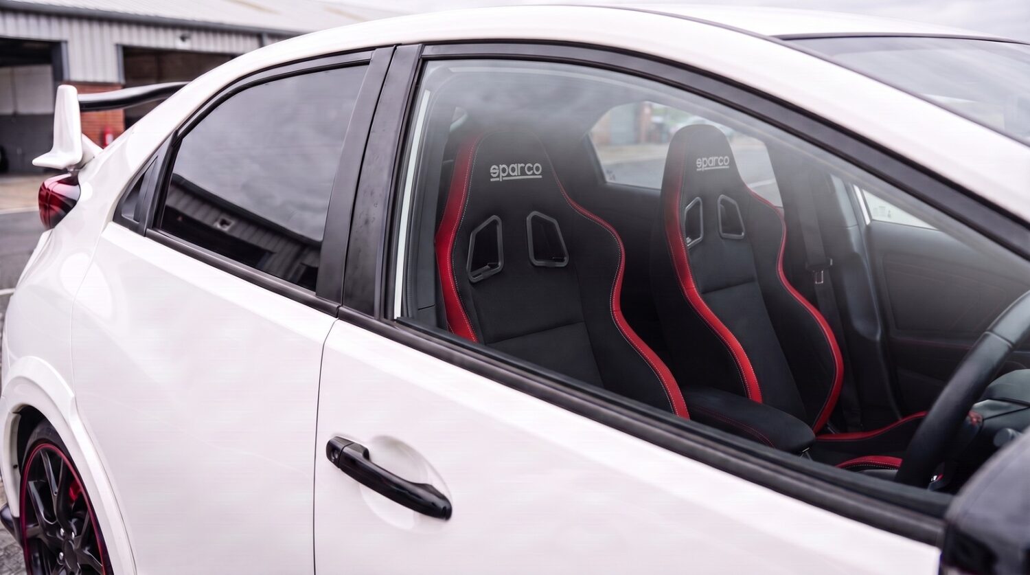 Pair of Sparco R100 reclining sports seats in black with red edge trim fitted in a Championship White 2015 Honda Civic Type R FK2, seen through the closed driver door window