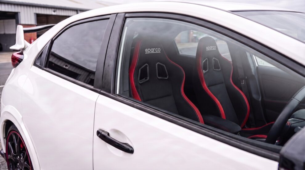 Pair of Sparco R100 reclining sports seats in black with red edge trim fitted in a Championship White 2015 Honda Civic Type R FK2, seen through the closed driver door window
