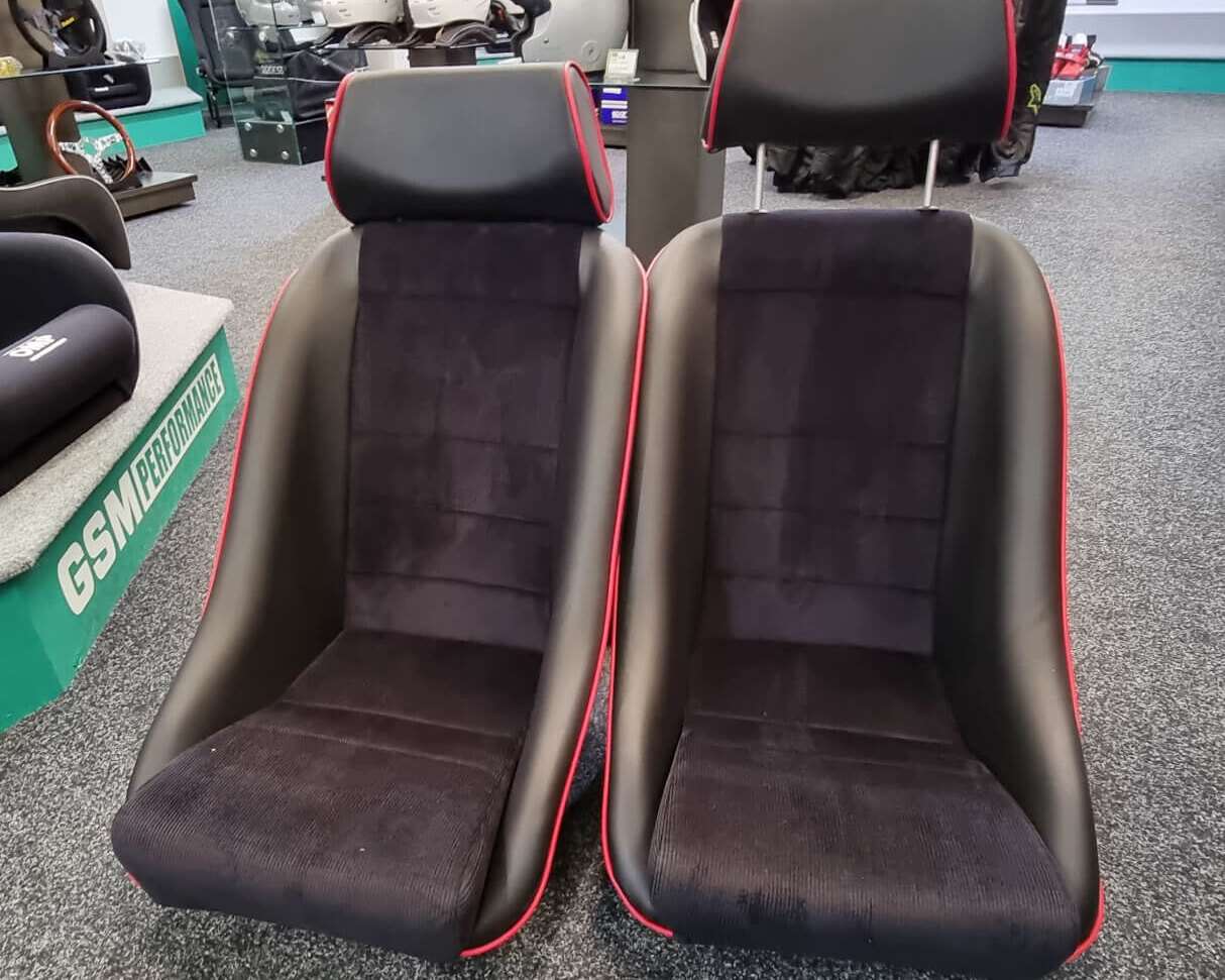 A pair of Cobra Classic GT bucket seats in black with red piping and headrests, on the showroom floor