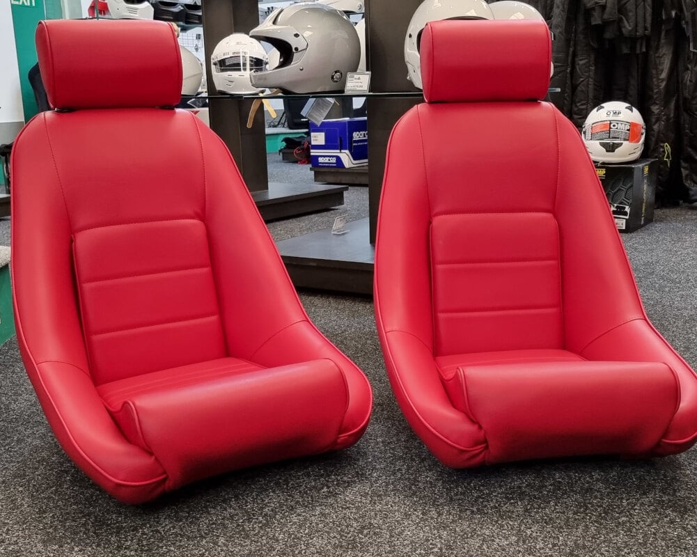A pair of Cobra Classic RS bucket seats trimmed in red vinyl with matching headrests, on the showroom floor