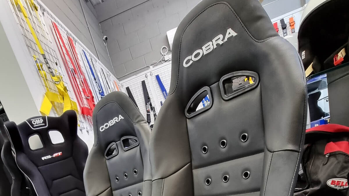 Two black Cobra Clubman 40th Edition bucket seats on the showroom floor beside the harness wall