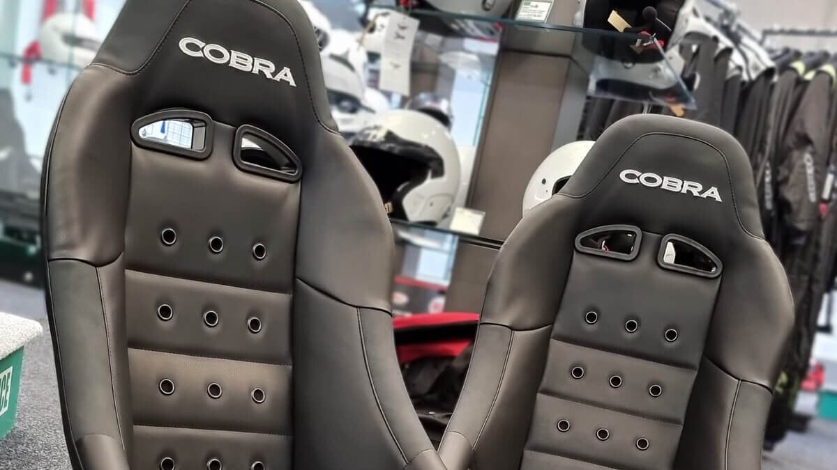 A pair of black Cobra Clubman 40th Edition bucket seats in front of the helmet shelves in the showroom