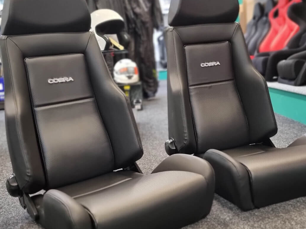 A pair of black Cobra Le Mans Carbon Edition reclining seats with carbon effect centre panels on the showroom carpet