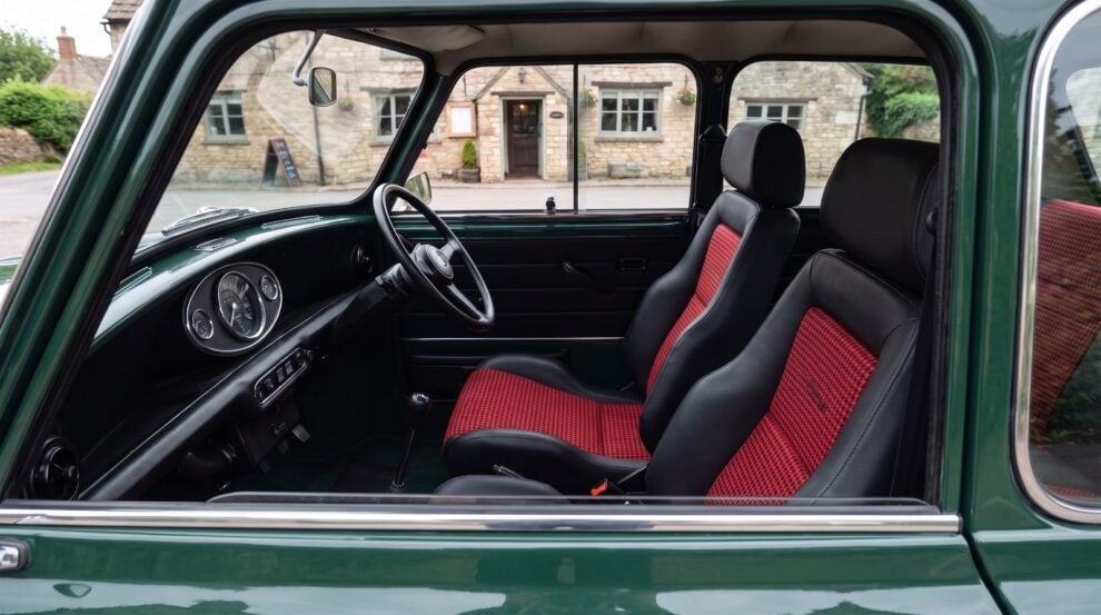 Looking down into the cabin of a dark green classic Mini over the top of the shut driver door, showing a Cobra Le Mans reclining seat in black vinyl with fine red and black houndstooth centre panels