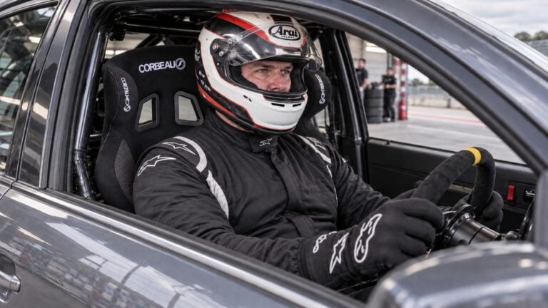 Broad-built helmeted driver checking the fit of a Corbeau Revenge X XL motorsport seat