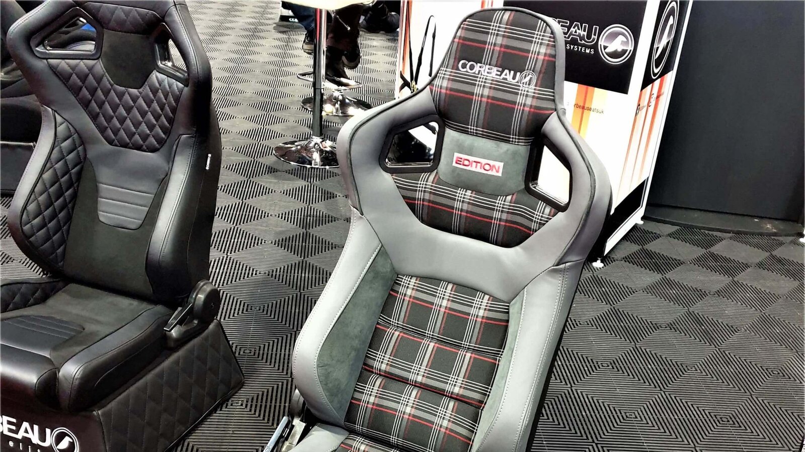 A Corbeau Sportline RRS Tartan Edition reclining seat in grey with red and white tartan on a Corbeau show stand