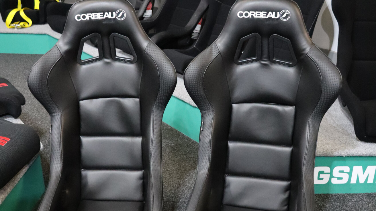 A pair of black vinyl Corbeau Sprint bucket seats on the showroom floor in front of the display plinth