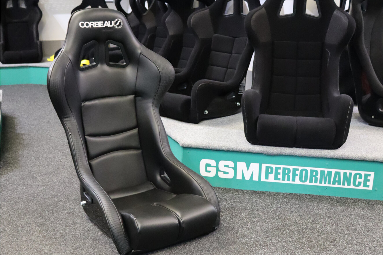 A black vinyl Corbeau Sprint X bucket seat on the showroom floor in front of the Corbeau fabric seat display