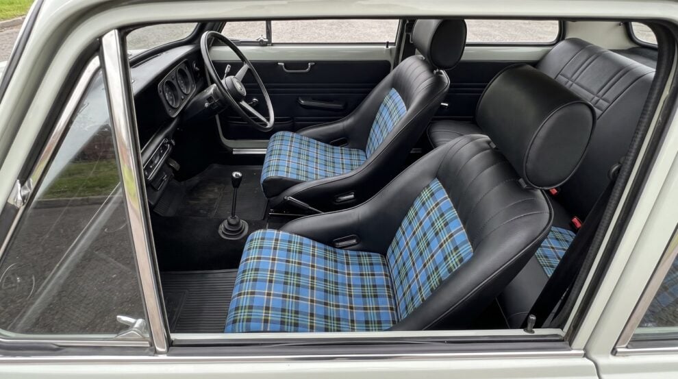Two Corbeau Classic Tartan Edition bucket seats in black with blue tartan centre panels, fitted in a restored nineteen seventies British saloon, seen through the wound down driver window over the top of the shut door