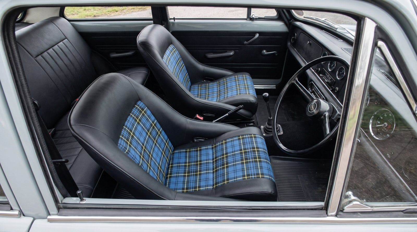 Two Corbeau Classic Tartan Edition bucket seats in black with blue tartan centre panels, fitted in a restored nineteen seventies British saloon, seen through the wound down driver window over the top of the shut door