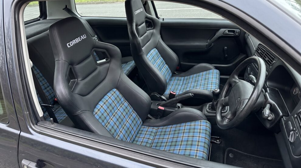 Two Corbeau Tartan Edition reclining sport seats in black with blue tartan centre panels, fitted in a nineties fast road hatchback, seen through the wound down driver window over the top of the shut door