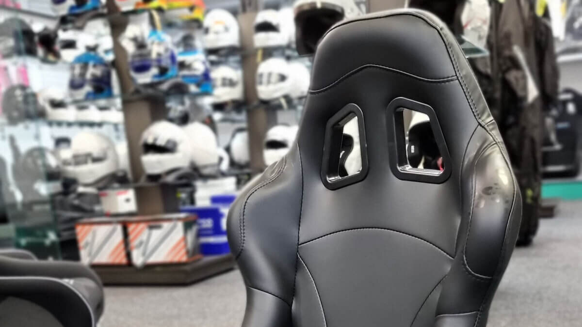 A black vinyl Endurance Motorsport First bucket seat in the showroom, with helmets on the shelves behind