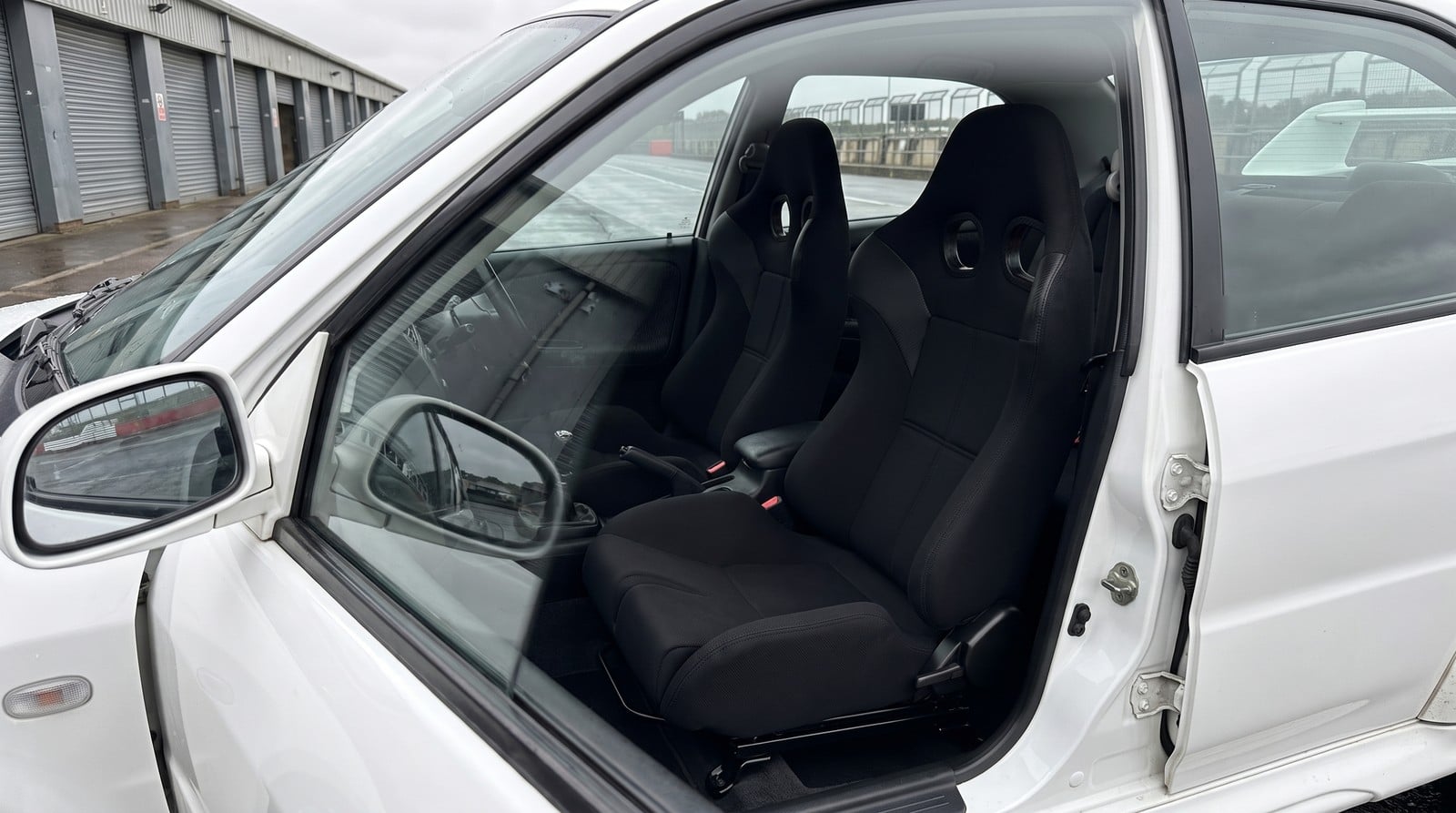 Pair of Corbeau PSR reclining sports seats fitted in a white 1999 Mitsubishi Lancer Evolution VI GSR, seen from the driver side in a circuit paddock