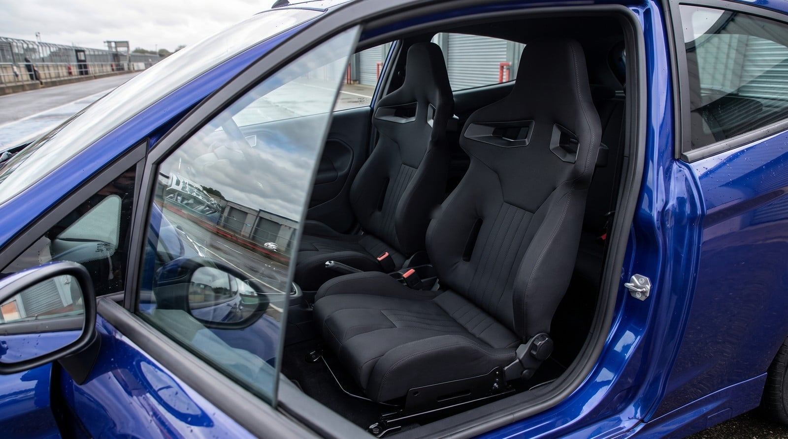 Pair of black Sparco R333 reclining sports seats fitted in a Spirit Blue Ford Fiesta ST180 Mk7, seen through the closed driver door window