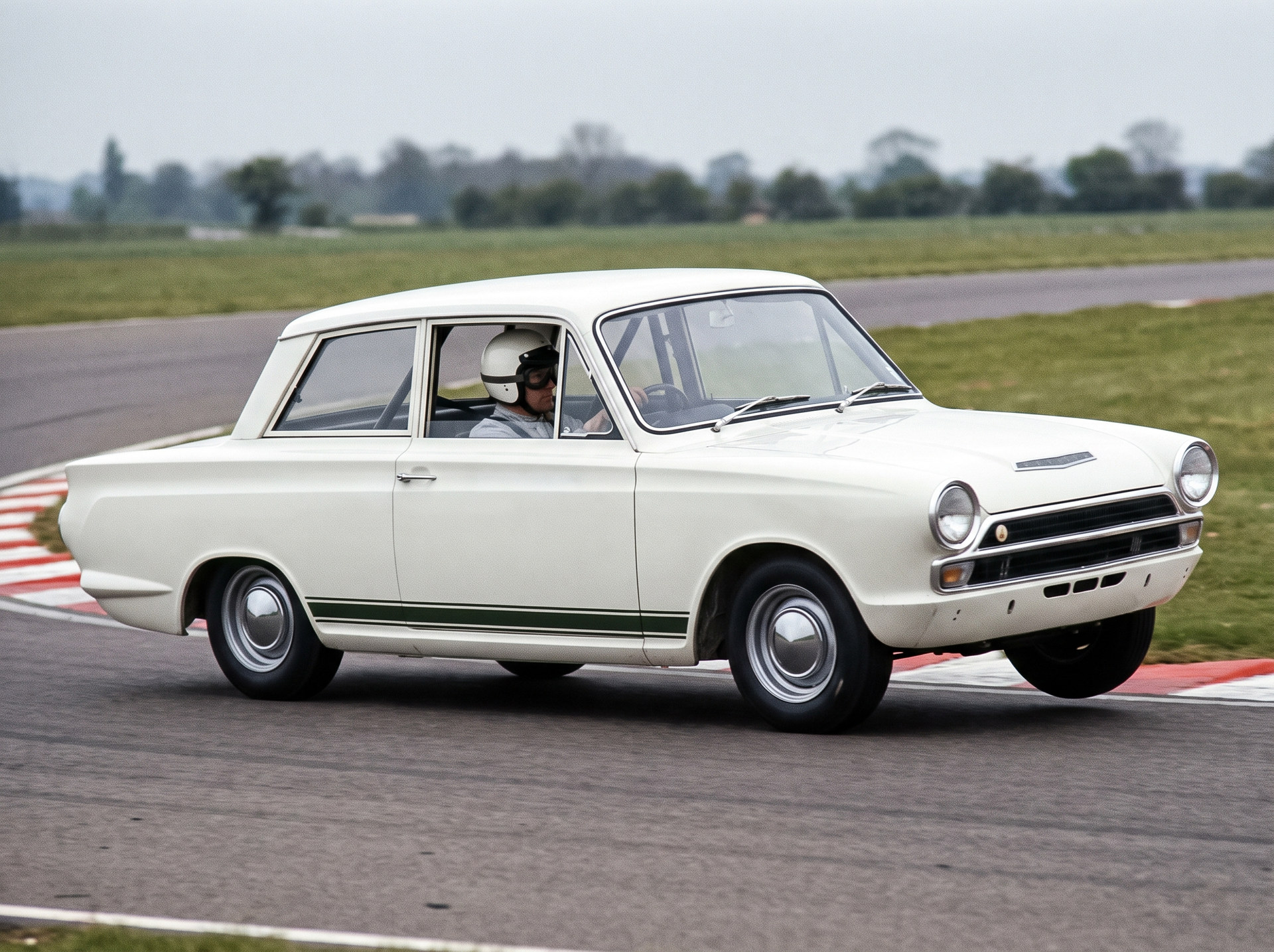 A white Ford Cortina Mk1 with a helmeted driver cornering on a British race circuit