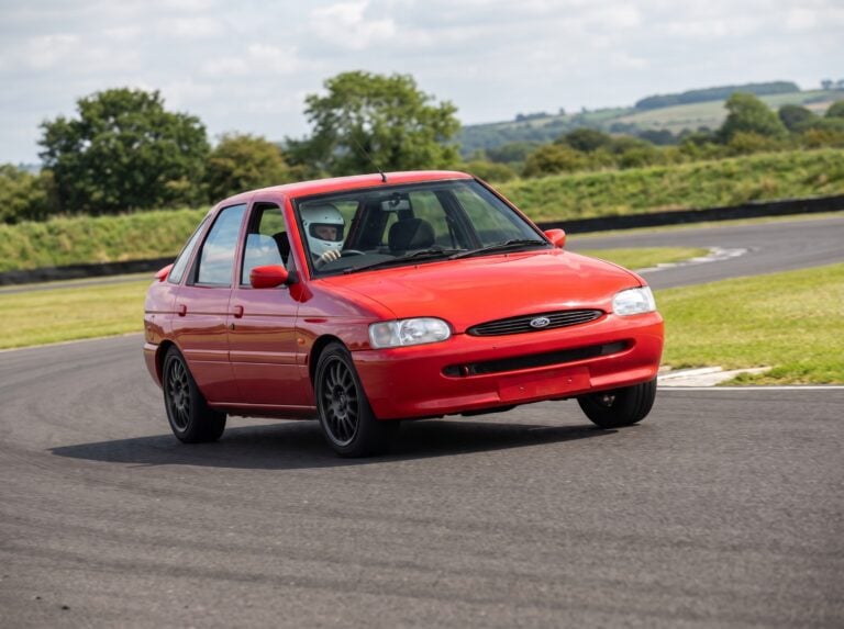 Ford Escort Mk7 cornering on a British race circuit, helmeted driver visible at the wheel