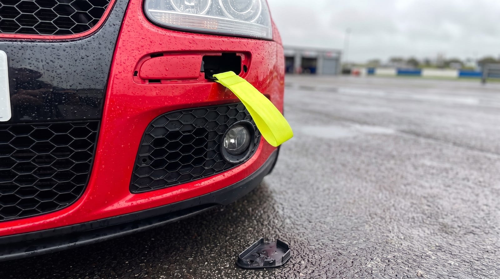 Hi-vis yellow fabric tow strap fitted through the front tow eye aperture of a red Volkswagen Golf GTI Mk5 in a circuit paddock