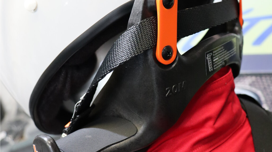 A HANS IV head and neck restraint on a white helmet and red race suit, with its tether running to the helmet
