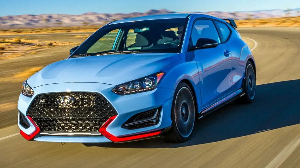 A light blue Hyundai Veloster N with red trim driving on a desert road