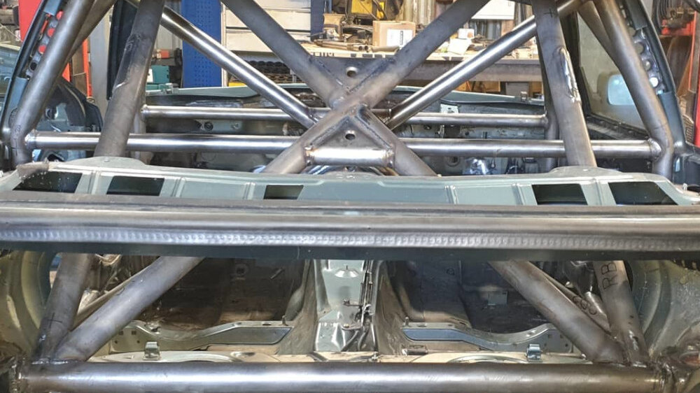 A bare steel JP Cages weld-in multipoint roll cage in a stripped BMW E36 Coupe shell, seen from the rear