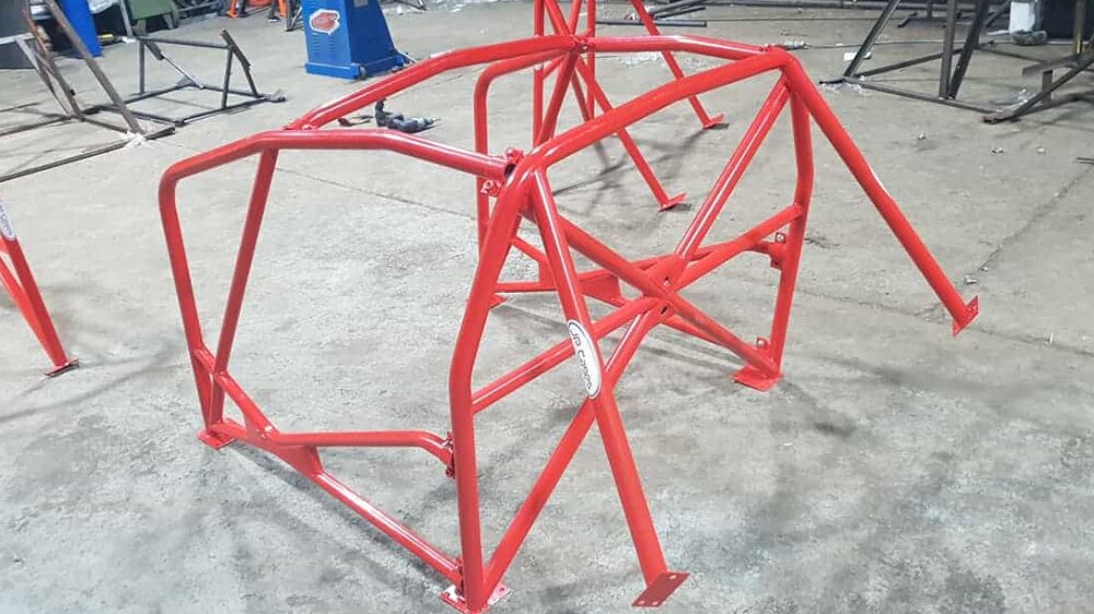 A red powder coated JP Cages multipoint roll cage for the Vauxhall Corsa D and E, standing on a workshop floor before fitting