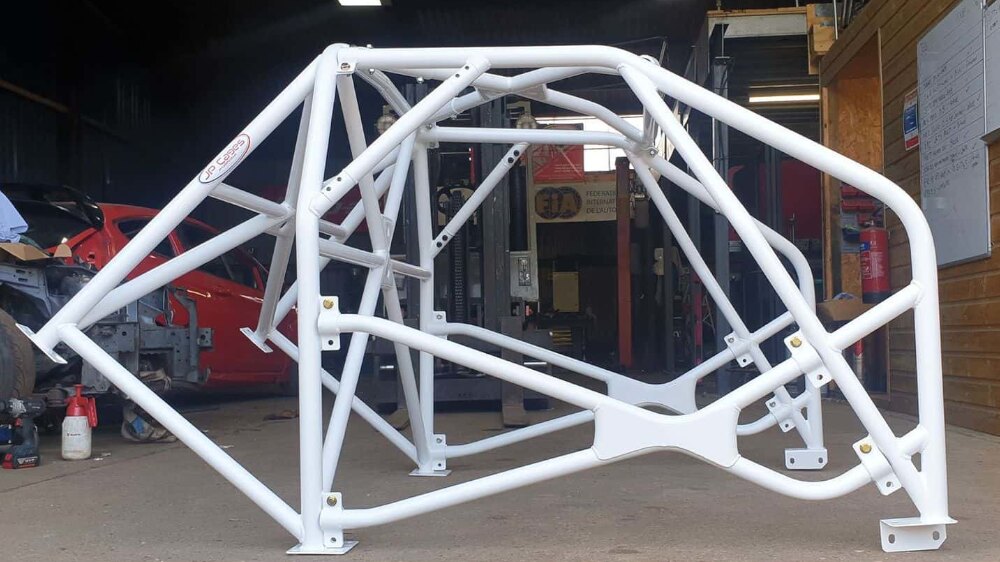 A white JP Cages JP7B competition roll cage for the Subaru Impreza standing on a workshop floor, with X bracing, diagonals and double door bars